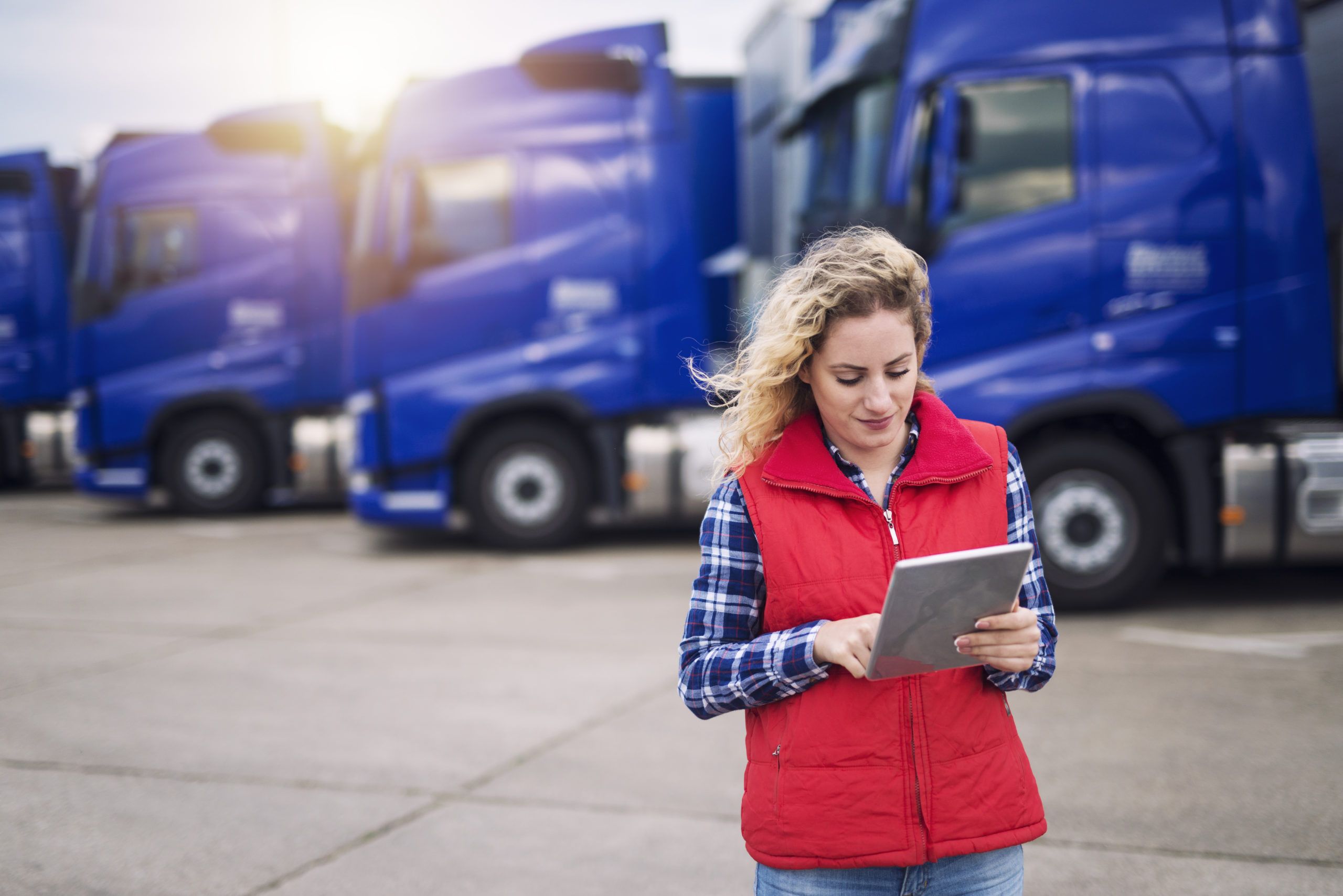 Truck driver holding tablet and checking route for new destination. In background parked truck vehicles. Transportation service.